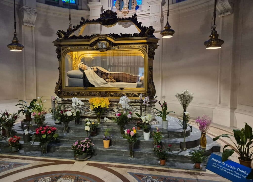 The life-sized marble recumbent statue of St. Thérèse of Lisieux in her Carmelite habit, lying peacefully with roses and a crucifix in her hands, located within a golden reliquary at the Carmel of Lisieux
