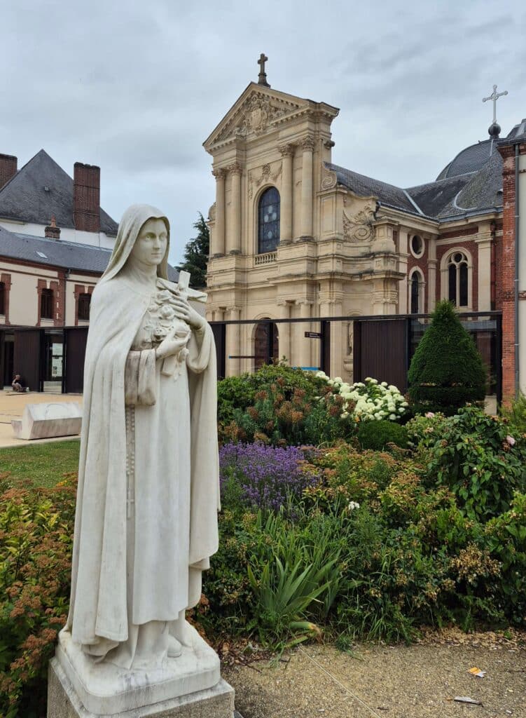 The modest, historic brick façade of the Carmelite Convent in Lisieux where St. Thérèse lived and died with her statue out front