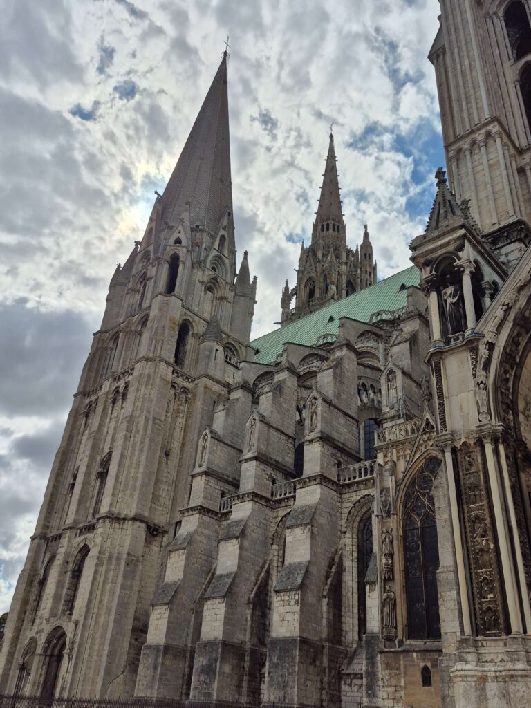 the two asymmetrical spires of Chartres Cathedral—one simple and Romanesque, the other ornate and Gothic—against a cloudy sky.