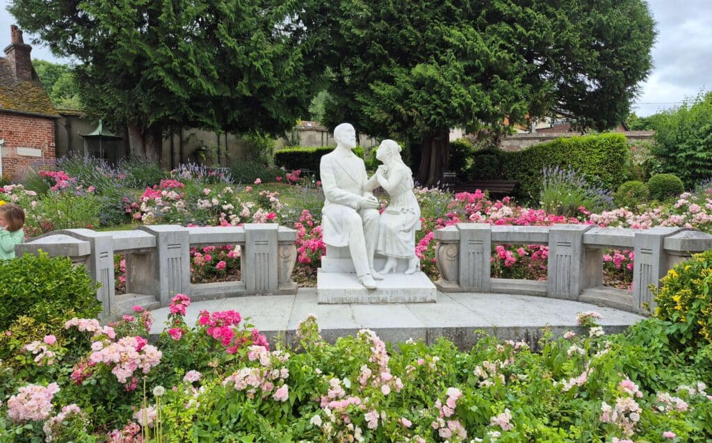 statue in a lush green garden depicting a young St. Thérèse of Lisieux sitting beside her father, Louis Martin, during their famous conversation about her vocation